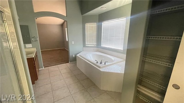 bathroom with tile patterned flooring, vanity, and a relaxing tiled tub