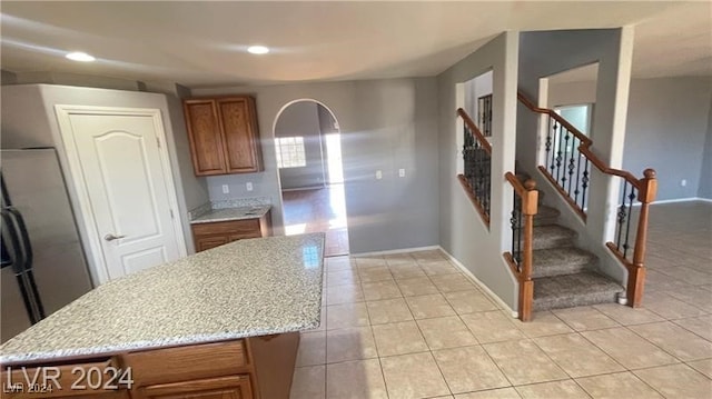 kitchen with a kitchen island, light tile patterned floors, light stone countertops, and stainless steel refrigerator