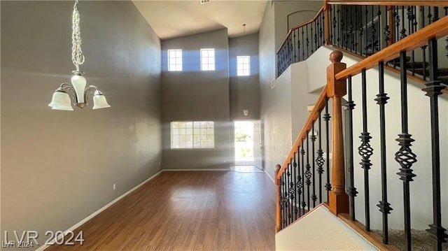 staircase with a healthy amount of sunlight, wood-type flooring, high vaulted ceiling, and a chandelier