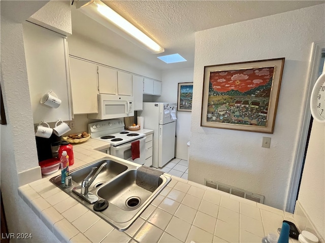 kitchen with tile countertops, white appliances, white cabinets, sink, and a skylight