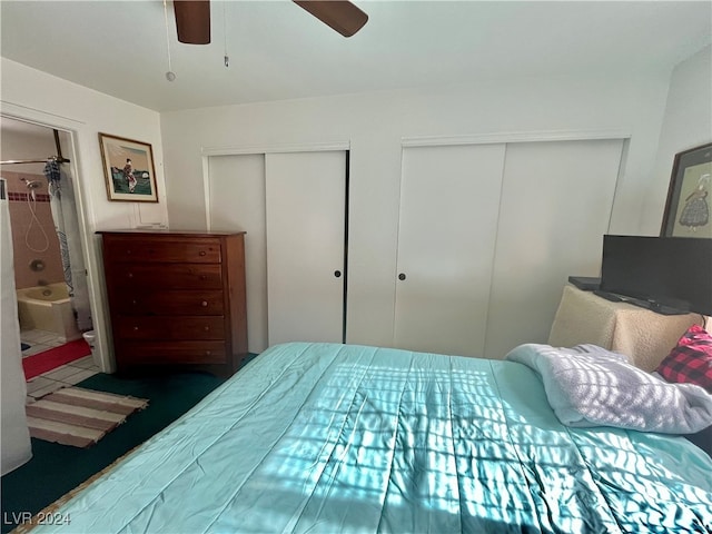 bedroom featuring dark colored carpet, ceiling fan, connected bathroom, and two closets