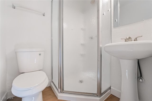 bathroom with toilet, a shower with door, and wood-type flooring