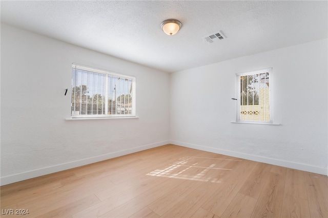 unfurnished room with a healthy amount of sunlight, a textured ceiling, and light hardwood / wood-style floors