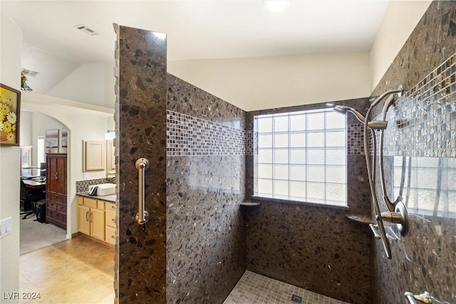 bathroom featuring vanity, vaulted ceiling, and a tile shower