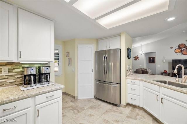 kitchen with sink, white cabinetry, tasteful backsplash, stainless steel fridge, and light stone countertops