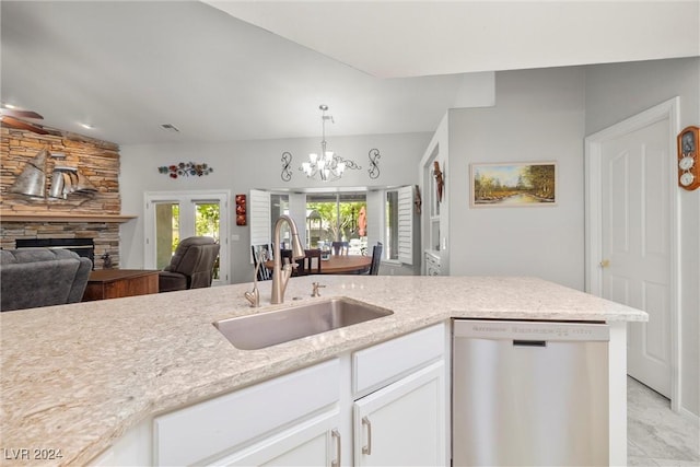 kitchen with pendant lighting, sink, dishwasher, white cabinets, and a stone fireplace