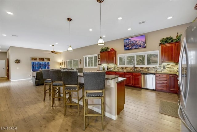 kitchen with sink, a breakfast bar area, ceiling fan, stainless steel appliances, and decorative backsplash