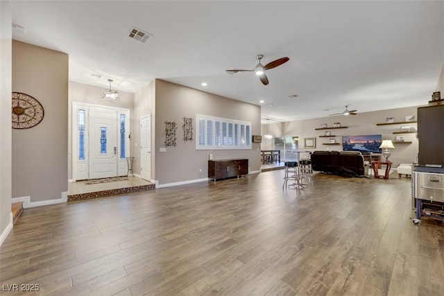 living area featuring visible vents, ceiling fan with notable chandelier, baseboards, and wood finished floors