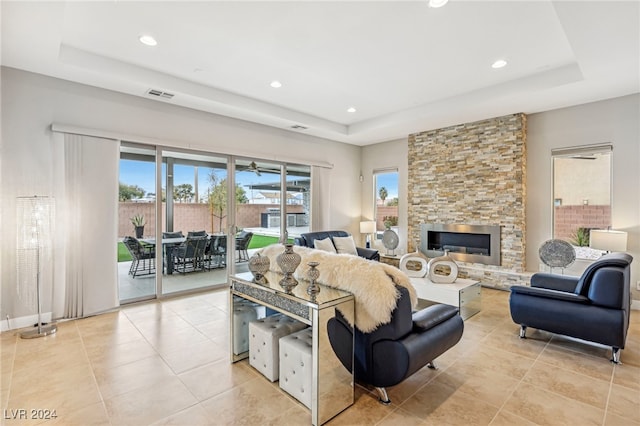 tiled living room with a raised ceiling and a stone fireplace