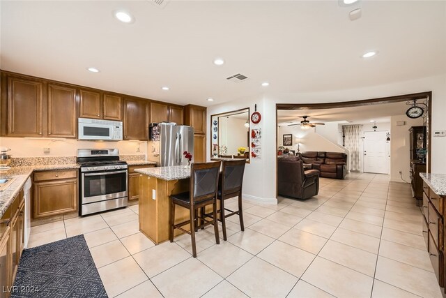 kitchen featuring light stone counters, a breakfast bar, stainless steel appliances, a center island, and light tile patterned flooring