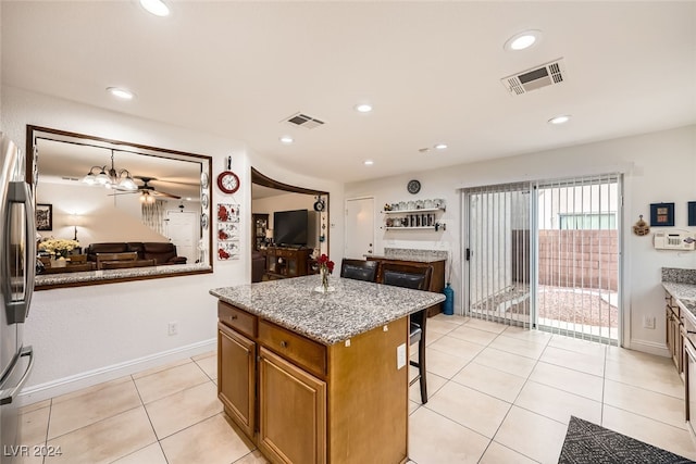 kitchen with ceiling fan, light tile patterned floors, light stone counters, a kitchen bar, and a kitchen island