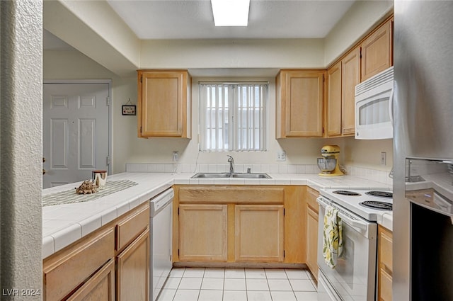 kitchen with tile countertops, white appliances, sink, light tile patterned floors, and light brown cabinetry