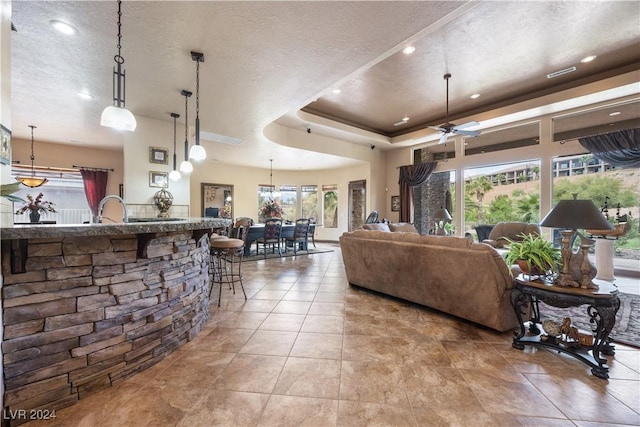 tiled living room featuring ceiling fan, sink, a textured ceiling, and a tray ceiling