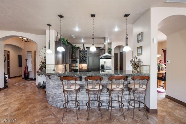 kitchen with pendant lighting, appliances with stainless steel finishes, ventilation hood, and kitchen peninsula