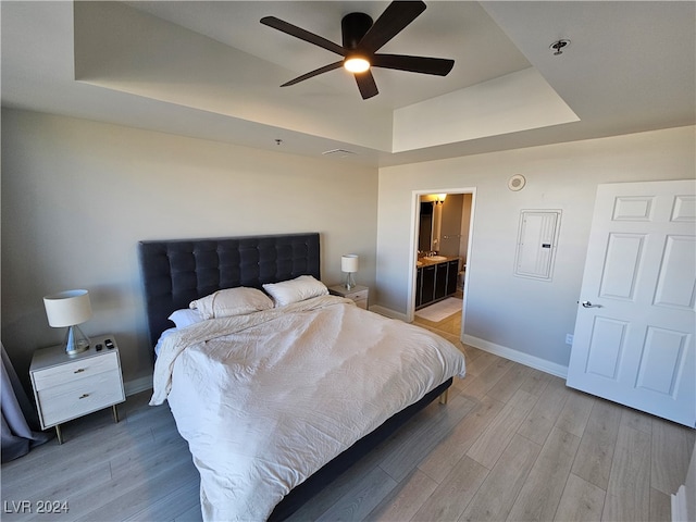 bedroom with ceiling fan, a raised ceiling, light wood-type flooring, and electric panel