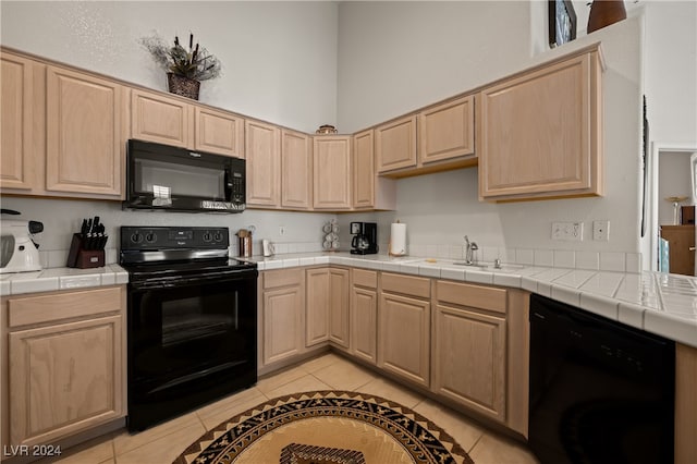 kitchen featuring light tile patterned floors, light brown cabinets, tile counters, and black appliances