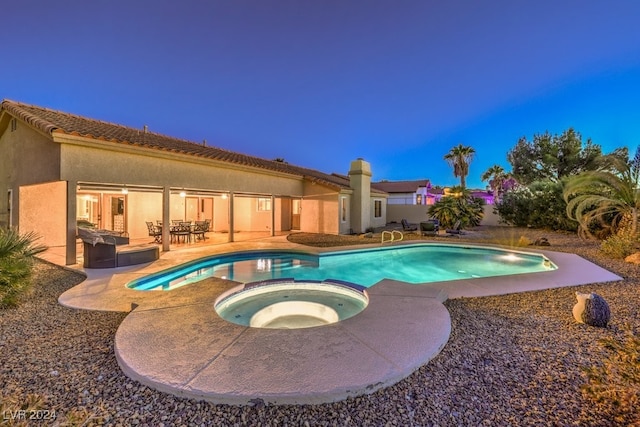 pool at dusk with an in ground hot tub and a patio area