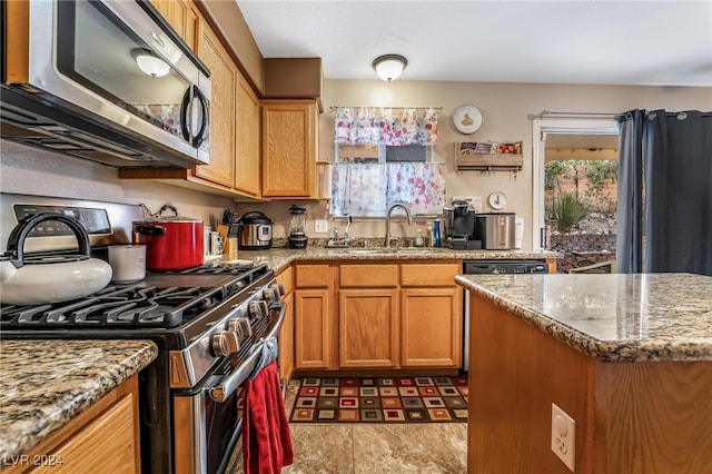 kitchen with a wealth of natural light, light stone countertops, sink, and appliances with stainless steel finishes