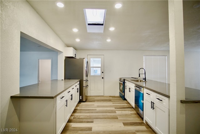 kitchen with kitchen peninsula, white cabinetry, a skylight, and appliances with stainless steel finishes