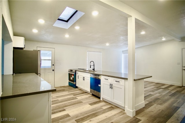 kitchen featuring white cabinets, sink, a skylight, light hardwood / wood-style flooring, and appliances with stainless steel finishes