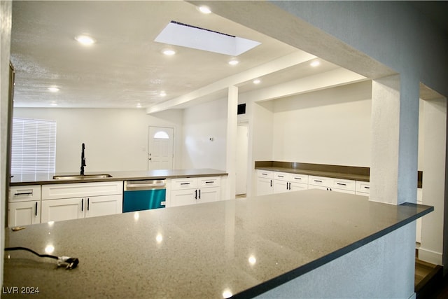 kitchen with sink, stainless steel dishwasher, vaulted ceiling with skylight, a textured ceiling, and white cabinetry