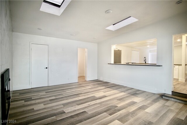 unfurnished living room featuring light hardwood / wood-style floors, sink, and a skylight