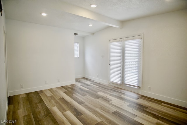 empty room with vaulted ceiling with beams, light wood-type flooring, a textured ceiling, and a wealth of natural light