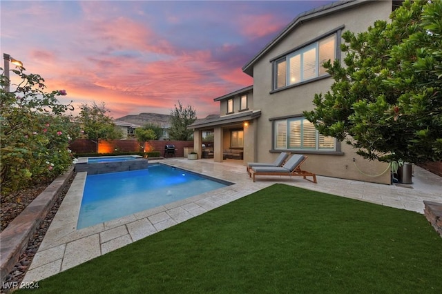 pool at dusk with a lawn, an in ground hot tub, and a patio