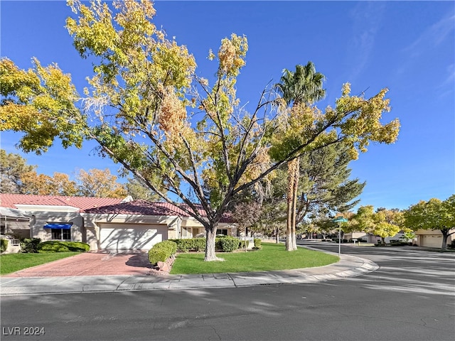 view of front of home featuring a garage, a tile roof, decorative driveway, a front lawn, and stucco siding