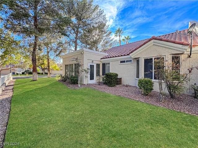 rear view of house with central air condition unit, a yard, a tiled roof, and stucco siding