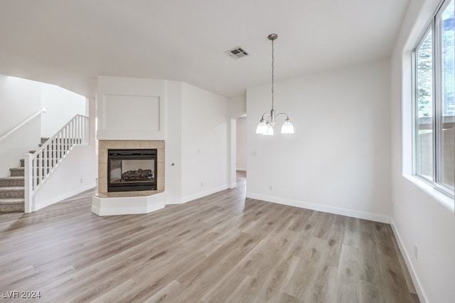 unfurnished living room featuring a multi sided fireplace, a notable chandelier, and light wood-type flooring