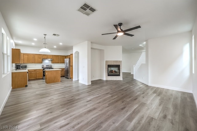 kitchen featuring appliances with stainless steel finishes, a tile fireplace, decorative light fixtures, light hardwood / wood-style flooring, and a center island