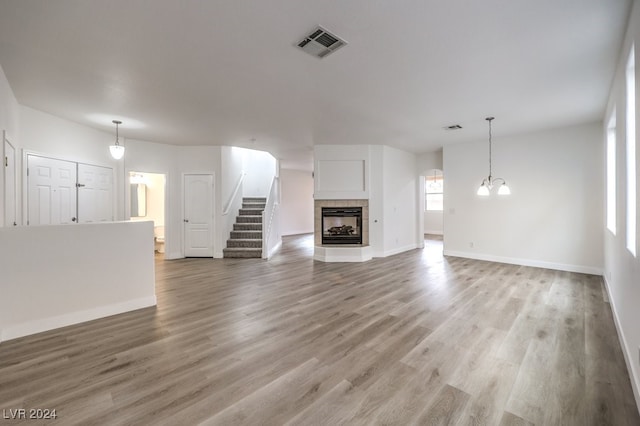 unfurnished living room with hardwood / wood-style floors, a notable chandelier, and a tile fireplace