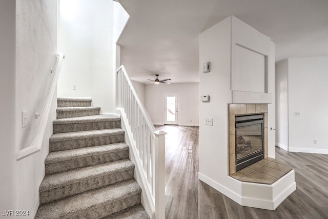 stairway featuring a tiled fireplace, ceiling fan, and hardwood / wood-style floors