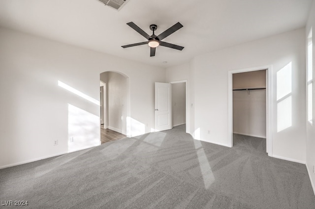 unfurnished bedroom featuring ceiling fan, a closet, a spacious closet, and dark colored carpet