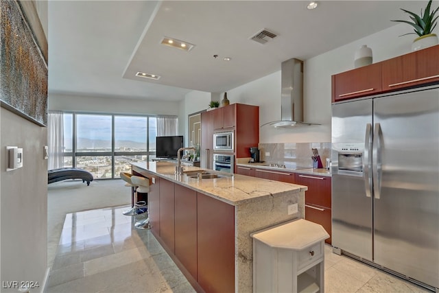 kitchen with appliances with stainless steel finishes, tasteful backsplash, sink, exhaust hood, and a center island with sink