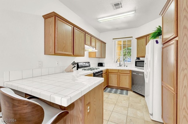 kitchen with tile countertops, sink, light tile patterned floors, kitchen peninsula, and stainless steel appliances