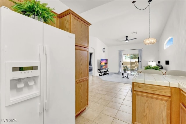 kitchen with ceiling fan, white refrigerator with ice dispenser, tile countertops, lofted ceiling, and light tile patterned floors