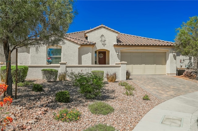 mediterranean / spanish house with a fenced front yard, a garage, a tile roof, decorative driveway, and stucco siding