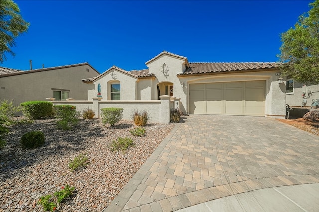 mediterranean / spanish home featuring a fenced front yard, an attached garage, a tile roof, decorative driveway, and stucco siding