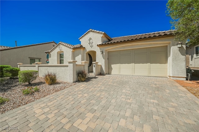 mediterranean / spanish-style house with a garage, decorative driveway, a tiled roof, and stucco siding