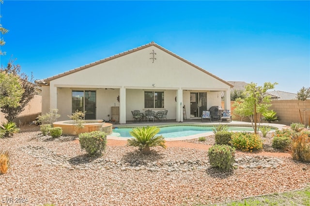 rear view of property featuring a fenced in pool, stucco siding, a patio area, an in ground hot tub, and a fenced backyard