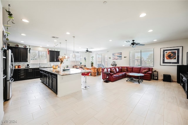 kitchen featuring light stone counters, dark cabinets, freestanding refrigerator, a center island, and decorative light fixtures