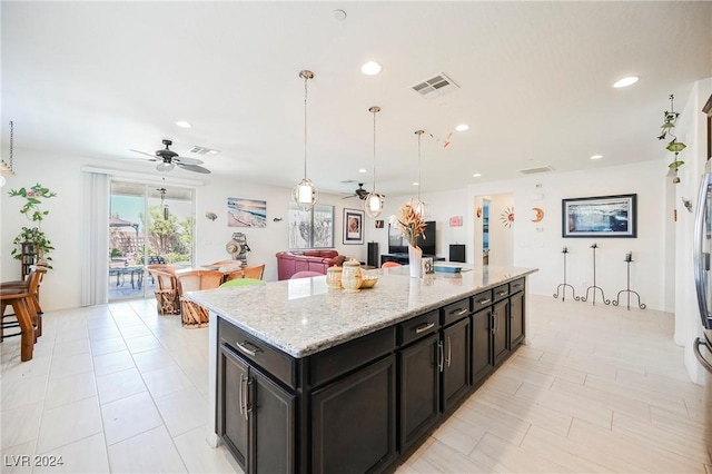 kitchen with a center island with sink, visible vents, a ceiling fan, decorative light fixtures, and light stone countertops