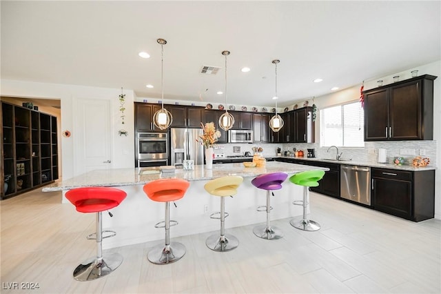 kitchen with a center island, a breakfast bar area, hanging light fixtures, appliances with stainless steel finishes, and a sink