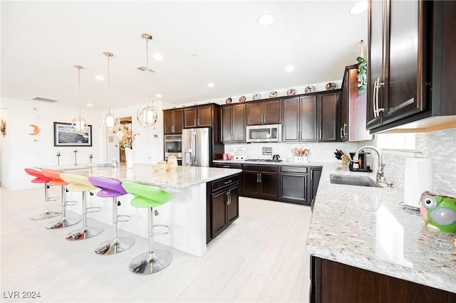 kitchen with appliances with stainless steel finishes, light stone counters, decorative light fixtures, a center island, and a sink