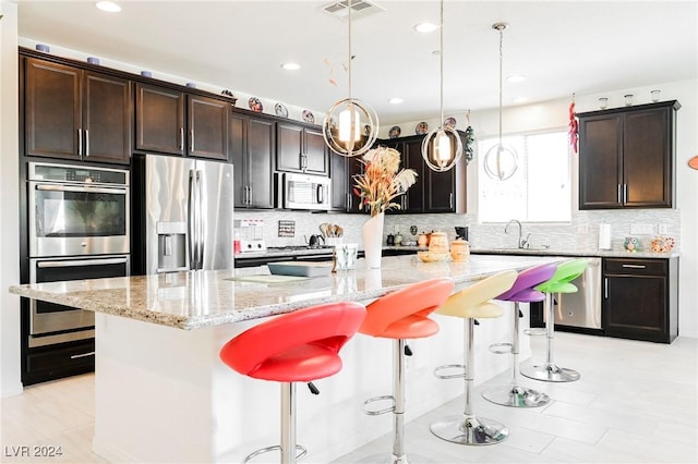 kitchen featuring visible vents, a kitchen island, a kitchen breakfast bar, hanging light fixtures, and stainless steel appliances