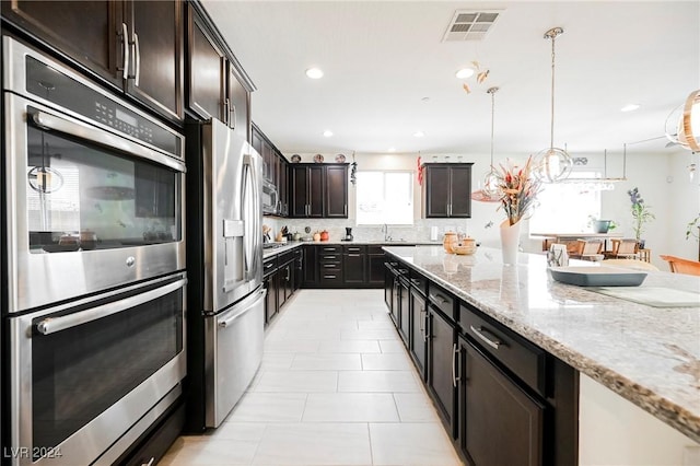 kitchen featuring stainless steel appliances, light stone counters, visible vents, and pendant lighting