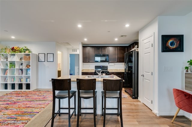 kitchen featuring a breakfast bar, black appliances, a center island with sink, light wood-type flooring, and dark brown cabinets