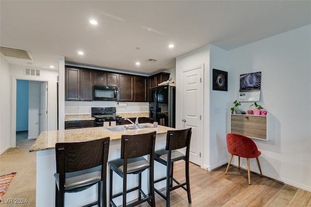 kitchen with a kitchen island with sink, black appliances, sink, light wood-type flooring, and a kitchen bar